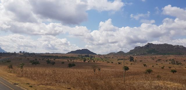 Open bush and rocky hills under big clouds beside the road.