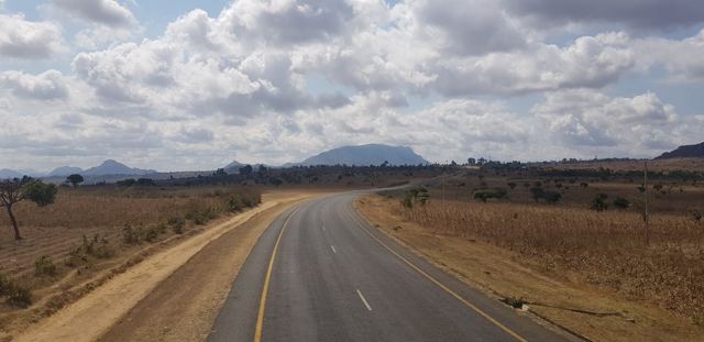 A long empty road running through dry bush towards distant hills.