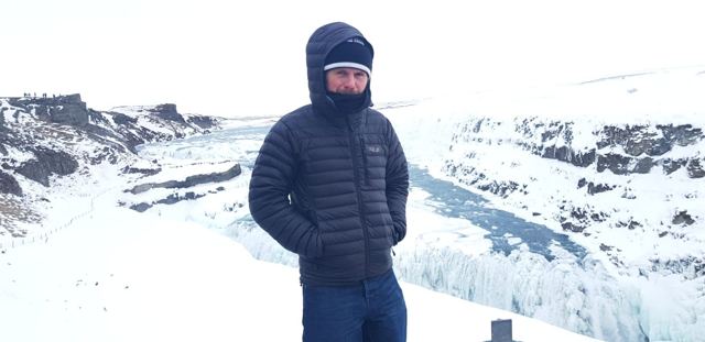 A man in a hooded down jacket in front of a snowy canyon and frozen waterfall in Iceland.