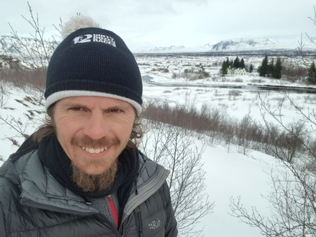 A smiling man in a beanie with snow-covered plains and mountains behind.
