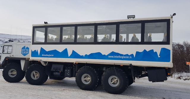 A large white eight-wheeled glacier truck with big windows parked on a snowy road.