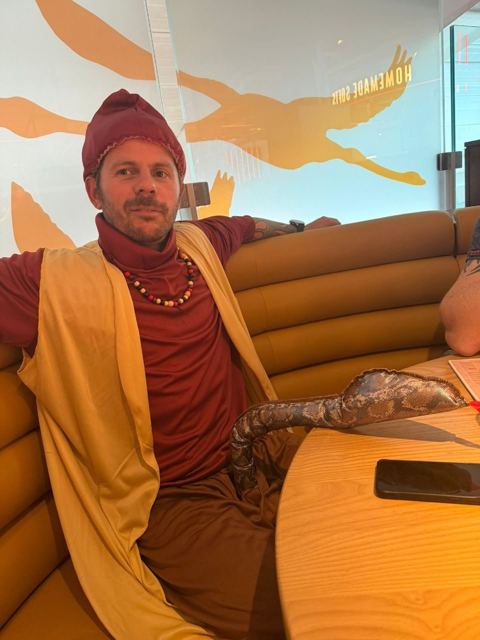 A man in a genie costume with a fez and robe lounging in an airport café.