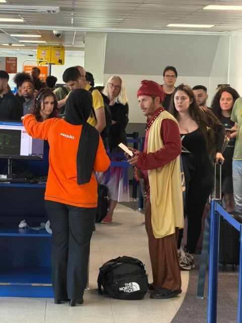 A man in a genie costume queuing at an airport check-in desk.