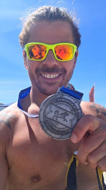 A grinning man in sunglasses holding up a large Spartan finisher medal.