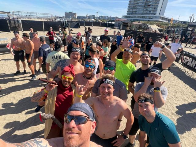 A large group of racers taking a selfie on the beach after a race.