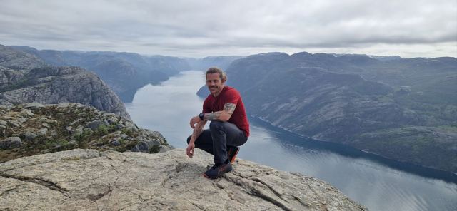 A man crouching on the flat top of Pulpit Rock with the fjord far below.