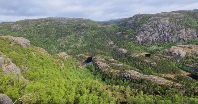 A green forested valley with granite hills and a small lake under a cloudy sky.