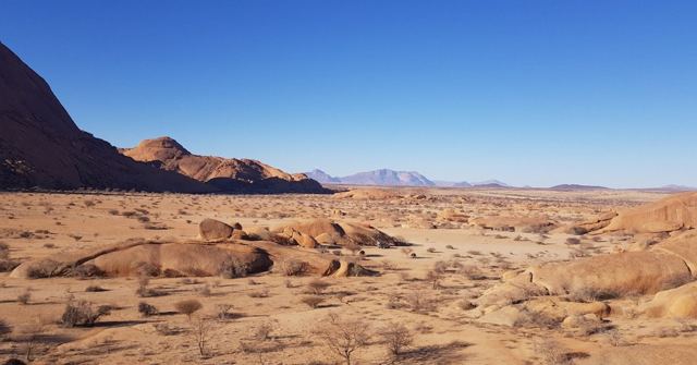 A desert landscape scattered with granite boulders and distant mountains.