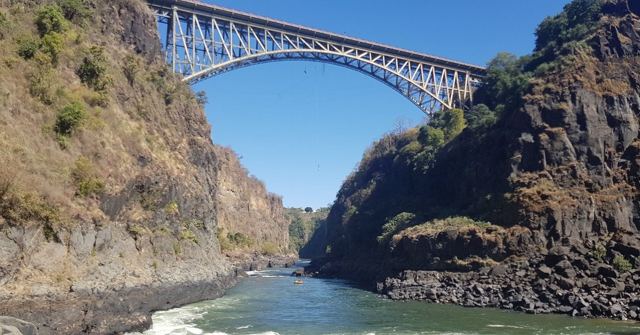 A steel arch bridge high over a deep rocky gorge with a river below.