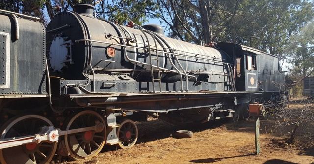 A large black steam locomotive on display outdoors under trees.