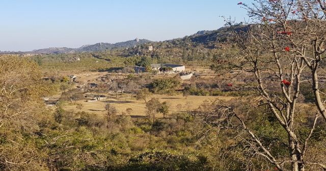 A view over a wooded valley with stone ruins and distant hills.