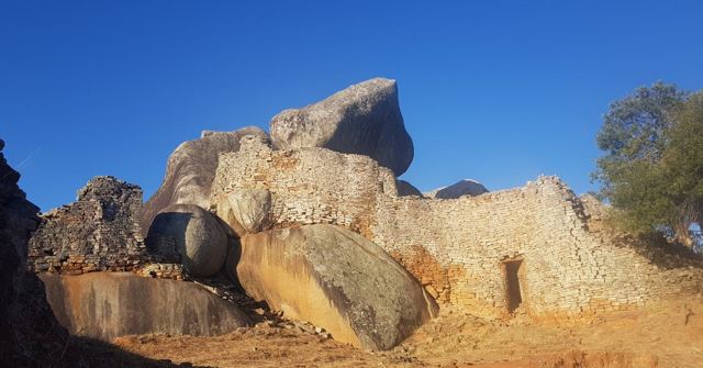 Ancient dry-stone walls built between huge granite boulders under a blue sky.
