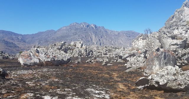 Jagged rocky mountains above a scorched plain scattered with pale boulders.