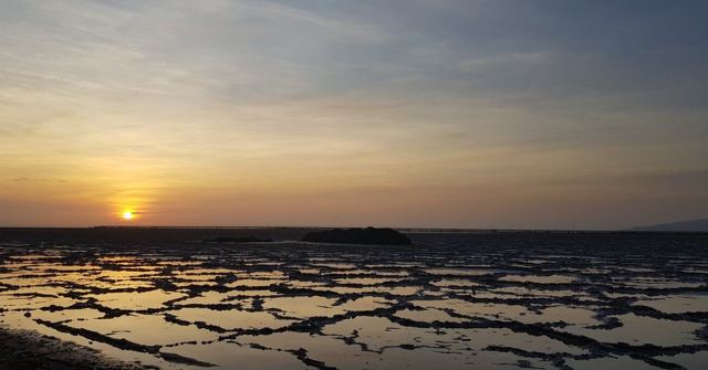 The sun low on the horizon over a patchwork of shallow salt pools.