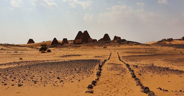 A row of small steep pyramids on orange desert sand with a stone path leading towards them.