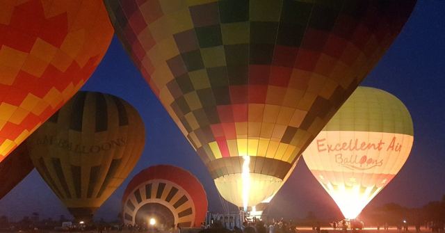 Close view of several glowing hot air balloons with checked and striped patterns against a dark blue sky.