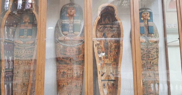 Several brightly painted ancient Egyptian sarcophagi displayed upright in glass cases.