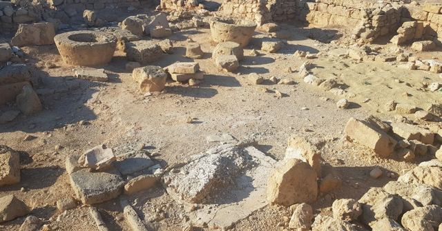 Scattered ancient stone ruins and foundations on dry, sunlit ground.