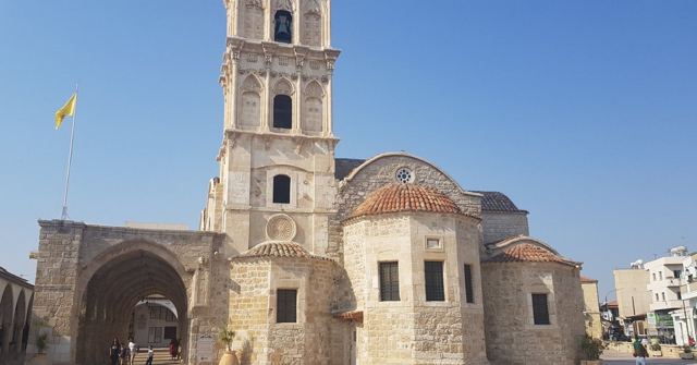 A stone church with a tall bell tower and domed roof under a clear blue sky.