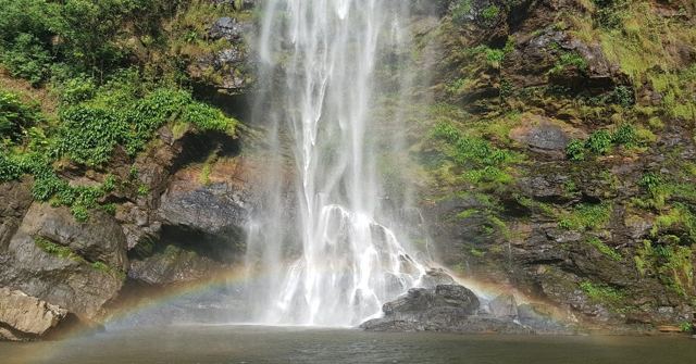 A tall waterfall falling down a rock face into a pool, with a rainbow at its base.
