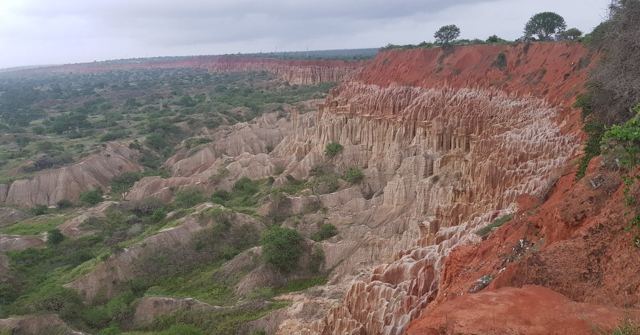 Steep red and cream eroded cliffs with green scrubland below.