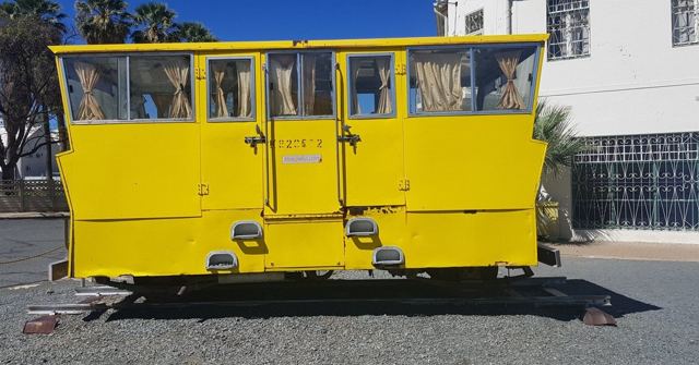 A bright yellow overland truck passenger cabin separated from its chassis, parked on gravel.
