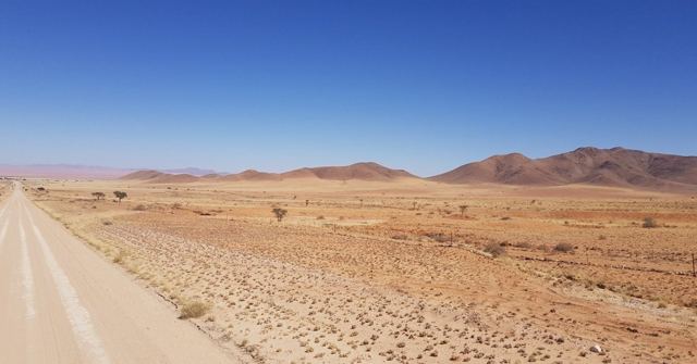 A straight gravel road through a red desert with mountains under a deep blue sky.