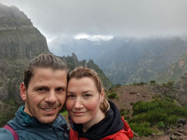 A man and a woman taking a selfie with jagged mountains and cloud behind.