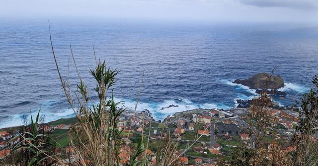Elevated view over a coastal village and a small rocky islet in a grey-blue ocean.