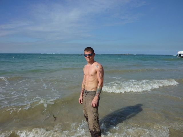 A man standing in shallow sea water on a beach in San Juan under a blue sky.