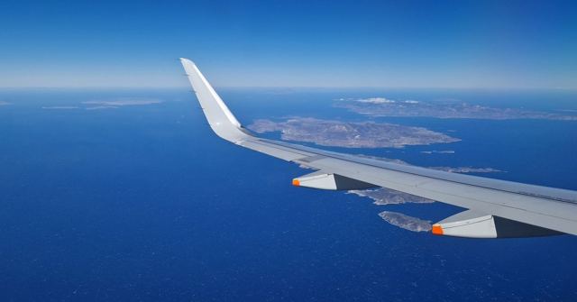 An aircraft wing over a deep blue sea with the islands of the Santorini caldera below.