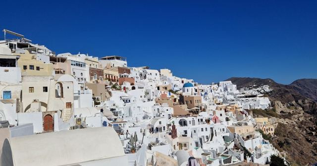 Whitewashed houses stacked along a cliff edge under a deep blue sky.