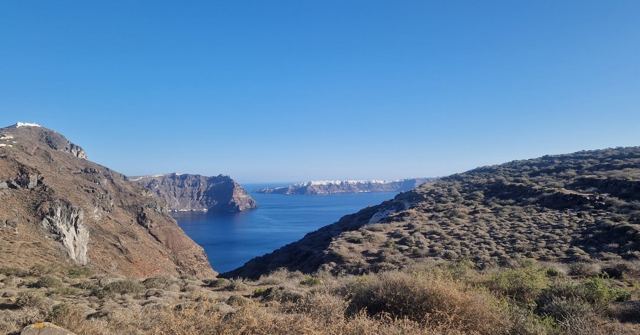 Dry, rugged hills sloping down to a deep blue bay under a clear sky.