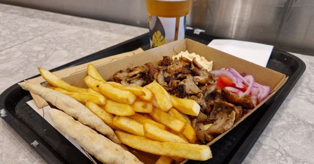 A tray of gyros meat with chips, pitta bread and salad on a table.
