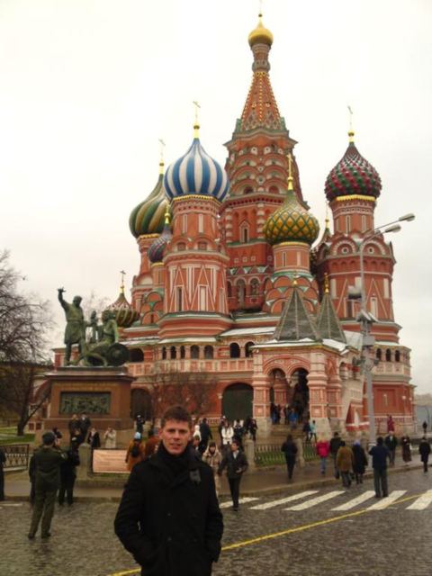 A man in a dark coat standing in Red Square in front of the colourful domes of St Basil's Cathedral.