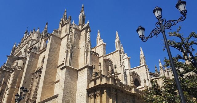 Ornate Gothic spires of Seville Cathedral beside a street lamp under a blue sky.