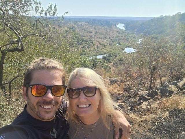 A man and a woman in sunglasses taking a selfie above a river valley.