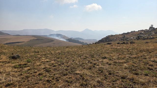 Golden grassland in the foreground with hazy mountains and drifting smoke in the distance.