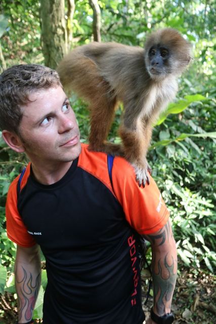 A man with a small monkey sitting on his shoulder in the jungle.