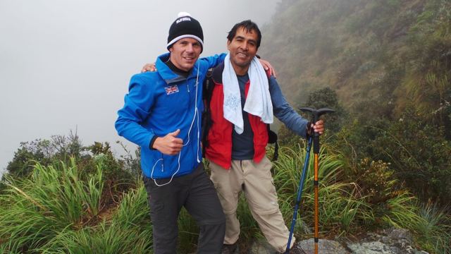 Two hikers in jackets smiling arm in arm on a misty trail in the Andes.