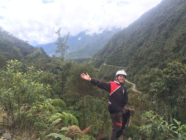 A man in a cycling helmet on a ledge above a deep green valley on the Death Road.