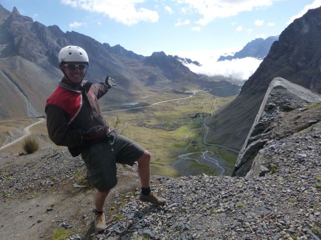 A man in a helmet pointing at a winding mountain road far below in the Andes.
