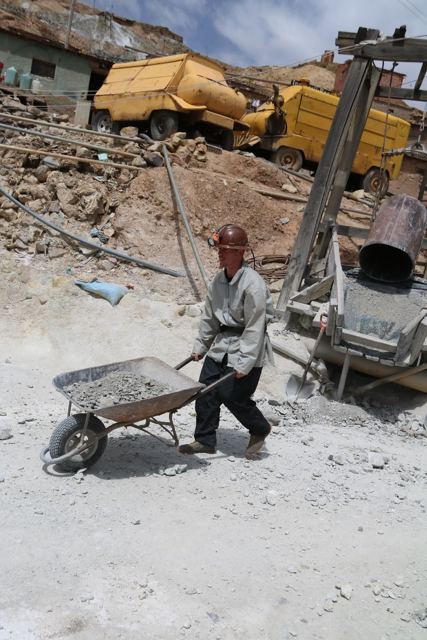 A man in a hard hat and overalls pushing a wheelbarrow of rock at a mine in Potosí.