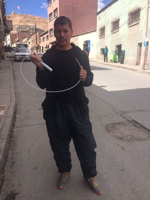 A man in miner's overalls holding a stick of dynamite and fuse on a street in Potosí.