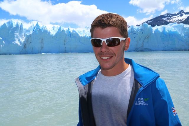 A smiling man in a blue jacket in front of the jagged blue ice wall of Perito Moreno Glacier.