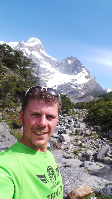A man in a green top taking a selfie in front of snowy mountains in Torres del Paine.