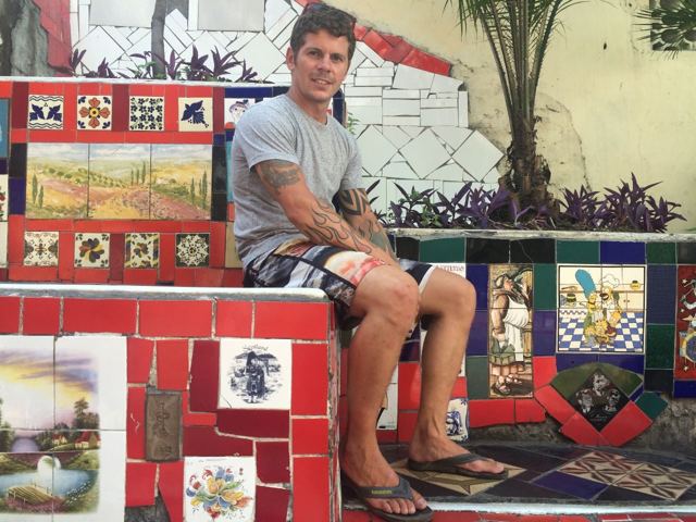A man sitting on brightly tiled steps covered in hand-painted tiles in Rio de Janeiro.