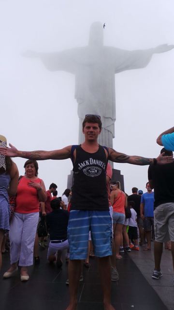 A man with arms outstretched in front of the cloud-shrouded Christ the Redeemer statue.