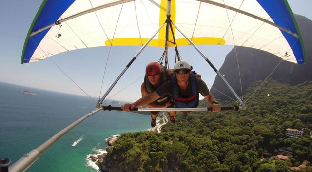 Two people tandem hang gliding over forest and coastline in Rio de Janeiro.