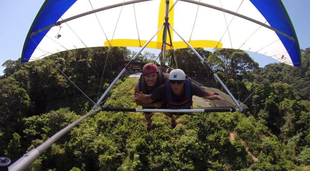 Two people hang gliding over thick green rainforest.